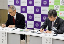 理事長と学長が協定書に手書き署名している様子