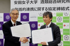 理事長と学長が協定書を手に取り、握手している様子